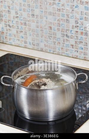 Faire mijoter le bouillon de poulet avec les légumes d'assaisonnement dans une casserole en acier sur une cuisinière vitrocéramique Banque D'Images