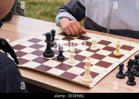 Un gros plan capture une partie d'échecs en cours sur une table en bois à l'extérieur. L'accent est mis sur le centre de l'échiquier roll-up, où le noir et Banque D'Images