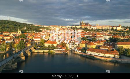 La lumière du matin jette une lumière chaude sur le pont Charles historique et le majestueux château de Prague. La rivière Vltava reflète l'architecture étonnante de la ville, créant une belle scène. Banque D'Images