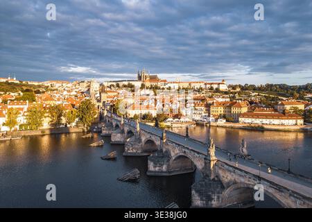 En début de matinée, la lumière du soleil baigne le château de Prague et le pont Charles, mettant en valeur l'architecture historique et le calme de la rivière Vltava. Une scène sereine se déroule dans la vieille ville de Prague. Banque D'Images