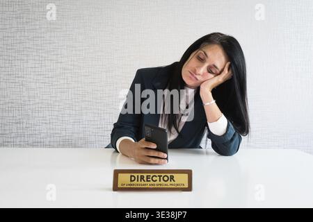 Jeune caucasien brunette femme d'affaires directrice dans le bureau s'assoir au bureau utiliser téléphone défilement nouvelles médias sociaux s'ennuyer au travail directeur drôle. Inutile em Banque D'Images