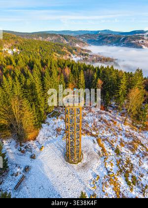 La tour de guet Svetly vrch est haute à Albrechtice, entourée d'arbres et de montagnes enneigés. Cette scène capture le paysage hivernal avec un ciel bleu clair et des collines lointaines. Banque D'Images