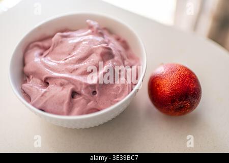 Assiette blanche colorée de crème glacée végétalienne à la banane mélangée avec des oranges sanguines avec des fruits de couleur rouge et violette Banque D'Images
