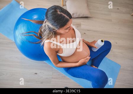 Femme enceinte se relaxant sur un tapis de yoga après l'exercice avec un ballon de gymnastique Banque D'Images