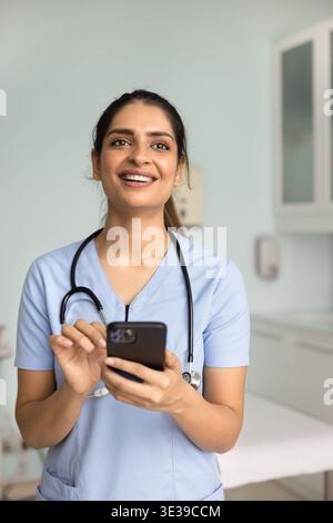 Jeune femme médecin confiante utilisant un smartphone debout à la clinique Banque D'Images