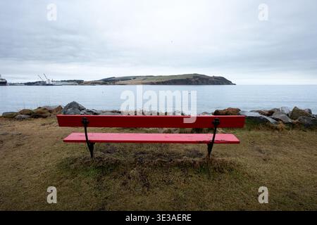Banc rouge surplombant Cromarty Firth à Cromarty, Highland, Écosse, avec une eau calme, un rivage rocheux et un ciel couvert. Banque D'Images