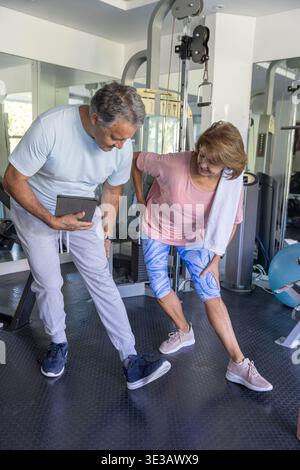 Femme senior et homme exerçant dans la salle de gym privée à domicile, tenant tablette et serviette, miroirs Banque D'Images