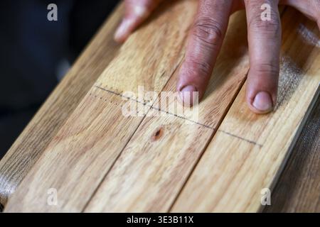 La main d'artisan focalisée avec les doigts sales marque des lignes précises sur la planche de bois pour le projet de travail du bois. Cette vue rapprochée montre le détail de la main-d'œuvre manuelle Banque D'Images