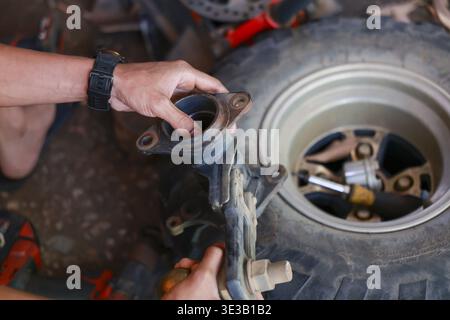 Homme concentré avec sa main réparant une suspension de roue de véhicule automobile. Ce mécanicien travaille sur vtt automobile avec concentration pendant la maintenance serv Banque D'Images
