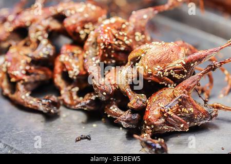 Cailles frites croustillantes assaisonnées d'ail et de graines de sésame, exposées dans un authentique stand de cuisine de rue thaïlandaise comme collation exotique de spécialités locales populaires. Banque D'Images