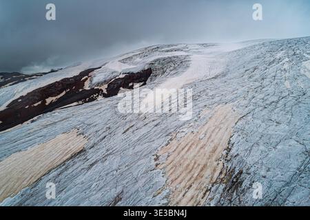 Aérien au-dessus du glacier épique fissuré Elbrus Caucasus montagne. Sommets enneigés dans les nuages de brouillard, fonte des glaciers. Banque D'Images