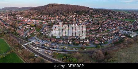 Vue aérienne panoramique d'un train de voyageurs à la gare de Helsby dans le Cheshire, en Angleterre, avec le village résidentiel et la colline de grès en arrière-plan. Banque D'Images
