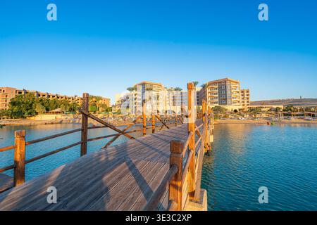 Un pittoresque quai en bois s'étendant au-dessus de la mer Rouge turquoise vers une station balnéaire de luxe à Hurghada, en Égypte, pendant un matin de printemps ensoleillé. Banque D'Images