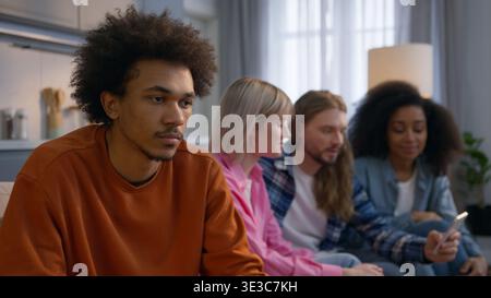 Homme afro-américain solitaire assis à la maison se sentant frustré mâle stressé isolé ignorant les amis caucasiens multiethniques femmes hommes discutant Banque D'Images