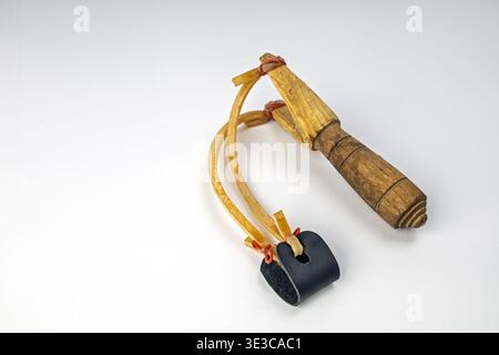 Gros plan d'une fronde rustique en bois faite à la main avec une poignée en bois tourné, des élastiques en latex jaune attachés avec un cordon rouge et une pochette en cuir noir Banque D'Images