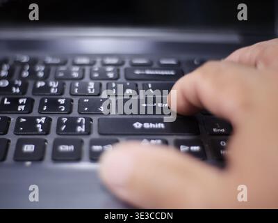 Image d'une main appuyant sur la touche 'entrée' d'un clavier noir d'ordinateur portable. Banque D'Images