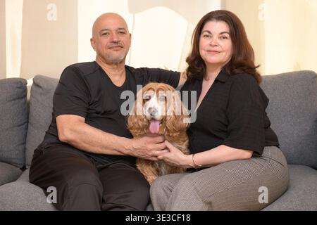 A man and woman sit on a couch holding a small brown and white dog indoors. Banque D'Images
