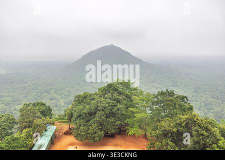 Sigiriya ancienne forteresse rocheuse au Sri Lanka. Vue panoramique sur une forêt tropicale luxuriante et verdoyante et une montagne lointaine sous un ciel couvert, brumeux, serein l Banque D'Images