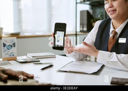 Femme asiatique d'âge moyen expliquant Mobile Banking App à la succursale bancaire Banque D'Images