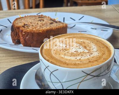 Gros plan d'un cappuccino chaud avec latte art à côté d'une tranche de pain à la banane Banque D'Images