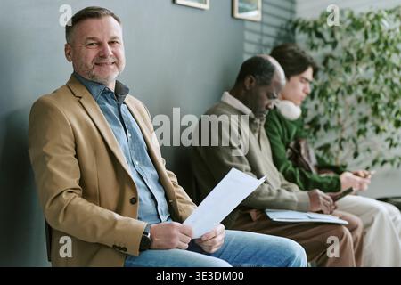 Portrait d'homme caucasien d'âge moyen souriant en attendant dans la succursale bancaire Banque D'Images