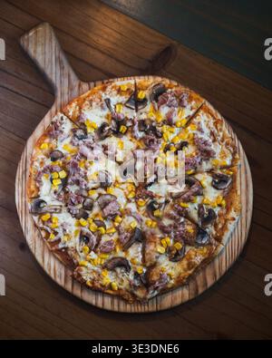 Pizza chaude au fromage garnie de maïs et de champignons. La planche en bois contient une pizza au charme rustique. La croûte dorée évoque la perfection fraîchement cuite. Cozy, moi Banque D'Images