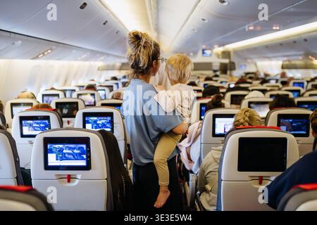 Maman calmant l'enfant bouleversé pendant le vol familial en voyageant dans l'avion. Banque D'Images