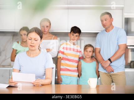 Mère bouleversée lit et regarde les documents financiers. Femme triste avec des enfants en arrière-plan Banque D'Images