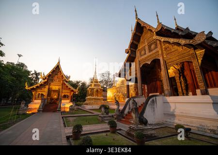 Chiang mai, Thaïlande – 5 mars 2020 : des édifices de temple ornés et un chedi doré sont vus dans le parc de Wat Phra Singh au coucher du soleil. Banque D'Images