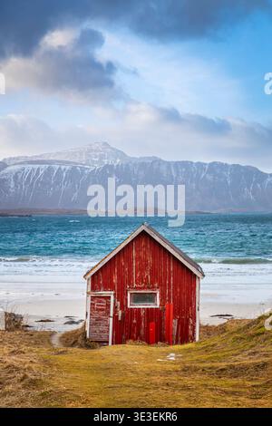 Cabane rouge typique sur la plage de Rambergstranda au coucher du soleil en hiver. Flakstadoya, Nordland, Lofoten, Norvège, Europe du Nord. Banque D'Images