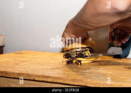 Mains arrangeant un hamburger double patty smash avec du fromage sur une surface en bois Banque D'Images