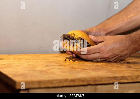 Mains tenant un hamburger smash fait maison avec des garnitures désordonnées sur une planche à découper en bois Banque D'Images