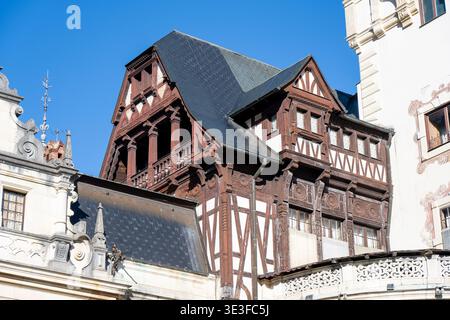 Gros plan de la façade supérieure ornée de bois et du balcon du château de Peleș à Sinaia, en Roumanie, contre un ciel bleu clair. Banque D'Images