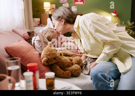 Femme d'âge moyen réconfortant enfant malade couché dans le lit à la maison Banque D'Images