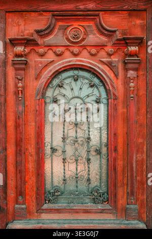 Porte en bois antique peinte en rouge avec cadre baroque sculpté élaboré avec rosette centrale, volutes, corbeaux décoratifs, pilastres tournés et sp Banque D'Images