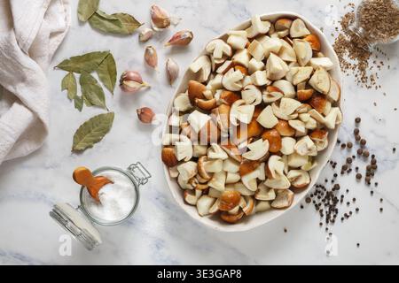 Champignons porcini frais crus tranchés dans une assiette blanche sur un fond de marbre. Les ingrédients de la marinade sont le sel, le poivre noir, la feuille de laurier, l'ail, le dil Banque D'Images