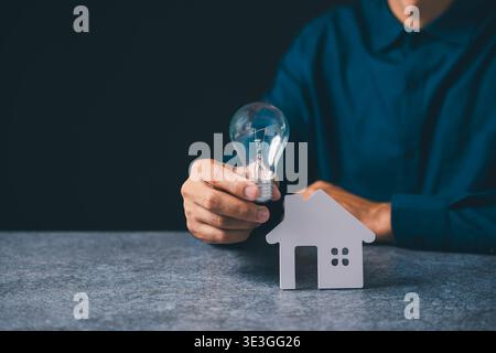 Main tenant l'ampoule près du modèle de maison pour l'innovation immobilière, idée d'énergie à la maison représentant l'épargne hypothécaire de propriété, kno d'électricité créative Banque D'Images