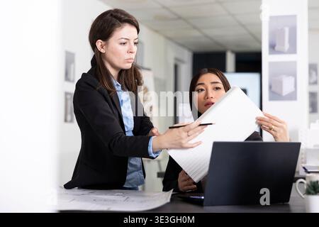 Divers professionnels féminins regardant le modèle de bâtiment 3D, recoupant avec les exigences du client sur ordinateur portable. Architectes asiatiques et caucasiens analysant le prototype dans le bureau pour le nouveau projet de construction. Banque D'Images