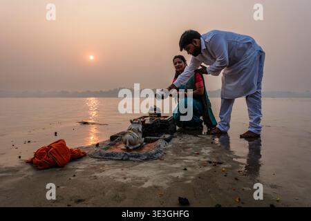 Un homme et une femme exécutent un rituel de l'eau sur un Shiva Lingam dans l'un des Ghats de Varanasi pendant le lever du soleil sur les rives du Gange. Banque D'Images