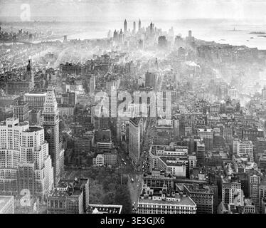 Cette superbe photographie aérienne en noir et blanc capture une vue panoramique du Lower Manhattan des années 1920, mettant en valeur le paysage urbain dense et les gratte-ciel emblématiques de l'époque. Le Flatiron Building et la Metropolitan Life Tower sont bien en vue, avec la Statue de la liberté faiblement visible dans la brume, capturant l'énergie animée du New York vintage. Banque D'Images