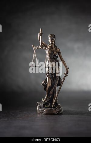 Une statue de bronze de Justice se dresse sur un fond sombre et texturé avec un éclairage latéral spectaculaire. La figure tient des échelles symbolisant la justice en un Banque D'Images