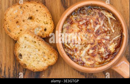 Soupe traditionnelle à l'oignon française avec baguette et fromage gruyère (emmental, comte ou beaufort) dans un bol en céramique sur fond de bois. Mise au point sélective Banque D'Images