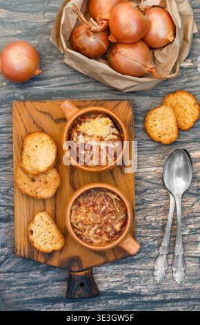 Deux portions de soupe traditionnelle à l'oignon française avec baguette et fromage gruyère (emmental, comte ou beaufort) dans des bols en céramique sur fond de bois. Banque D'Images