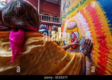 Une femme dans un saree lumineux touche une murale vibrante d'une divinité sur un mur de rue dans le centre historique de Varanasi près de Vishvanath Mandir. Banque D'Images
