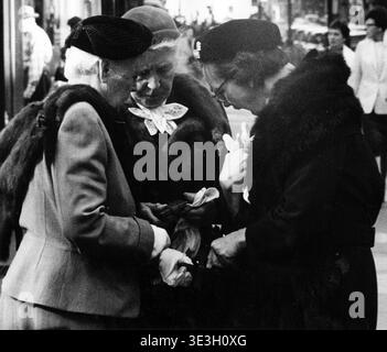 Trois femmes âgées, vêtues de manteaux et de chapeaux à la mode caractéristiques de l'époque, se blottissent ensemble sur ce qui semble être un trottoir de New York dans cette photographie de rue intime en noir et blanc d'Angelo Rizzuto des années 1950 Ils semblent être engagés dans un moment partagé, examinant peut-être quelque chose dans leurs mains ou leurs sacs, capturant un aperçu franc de la vie quotidienne et de la connexion personnelle dans un cadre urbain. Banque D'Images