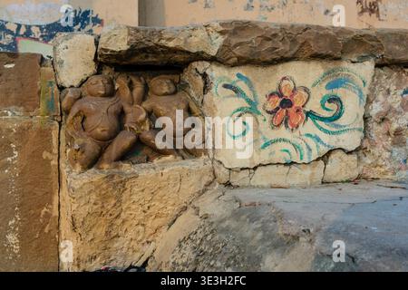 Gros plan d'anciennes sculptures religieuses en pierre et d'une peinture florale moderne sur un mur d'un ghat Varanasi situé le long de la rive du Gange. Banque D'Images