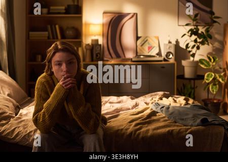 Portrait d'une adolescente assise sur le lit pensant dans une chambre confortable Banque D'Images