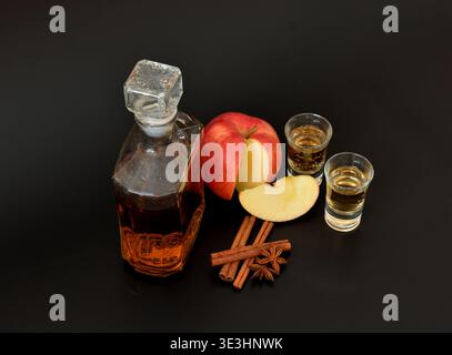 Une bouteille et deux verres de liqueur de pomme à la cannelle et à l'anis sur fond noir. Gros plan. Banque D'Images