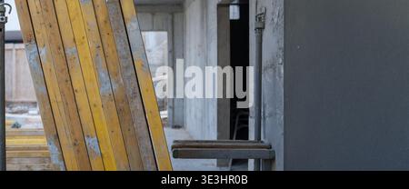Des planches de bois reposent contre un mur sur un chantier de construction. Le bâtiment est en cours, avec des murs en béton non finis et des outils dispersés aro Banque D'Images