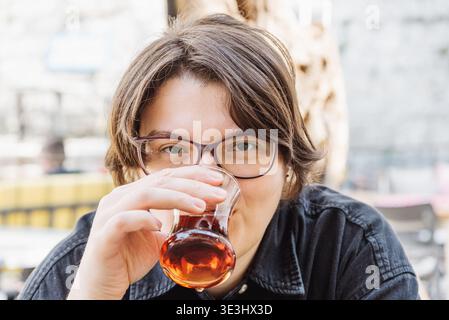 Jeune femme buvant la boisson de thé noir de tasse en verre traditionnel mug turc armud dans le café en vacances Banque D'Images